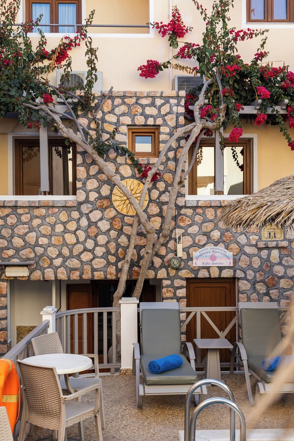 Un bâtiment en pierre doté d’un balcon, d’un espace extérieur aménagé pour s’asseoir et d’un arbre aux fleurs rouges.