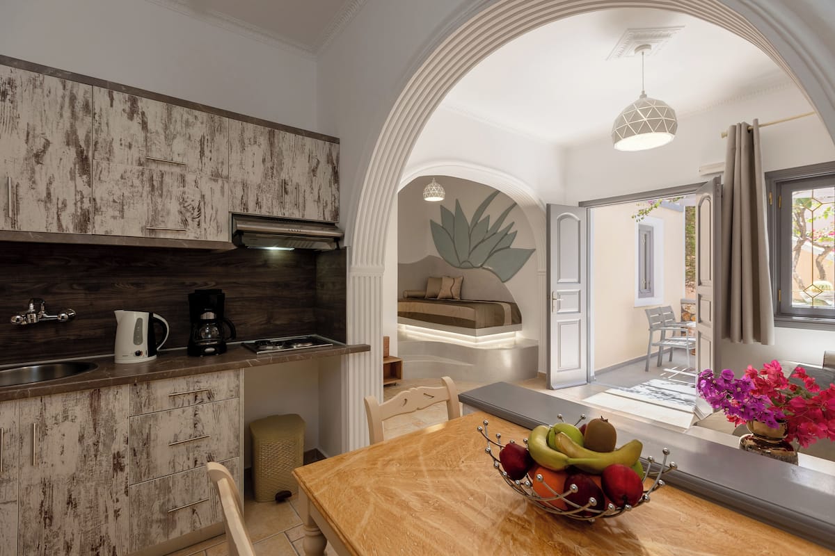 A modern kitchen with a rustic wood backsplash, a dining area with a wooden table, and a cozy seating area with a sofa and a large leaf wall decoration.