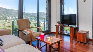 Un saló modern amb un televisor gran, seients còmodes i una vista panoràmica d'un paisatge de muntanya a través de grans finestres.