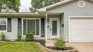 Une maison de plain-pied avec un garage, un porche à l’avant et un petit jardin devant, agrémenté d’un parterre de fleurs.