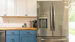 Une cuisine avec un réfrigérateur en acier inoxydable, des armoires bleues et un plan de travail en bois.