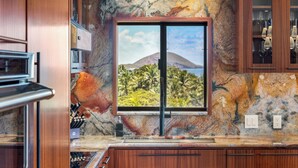A kitchen with a large window, wooden cabinets, and a marble backsplash.