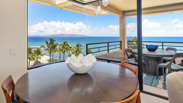 A dining area with a view of the ocean, a large white bowl on the table, and a blue bowl on the balcony.