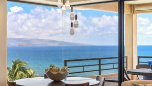 A dining area with a view of the ocean, a round table, chairs, and hanging light fixtures.