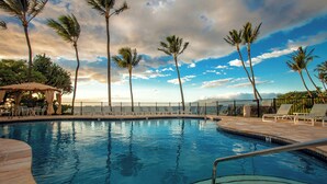A swimming pool with lounge chairs and palm trees, surrounded by a fence and a view of the sky.