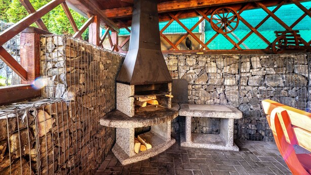 Un área de cocina al aire libre de estilo rústico, con un muro de piedra, una chimenea grande y una mesa de madera.