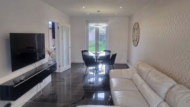 A modern living room with a flat-screen TV, a sofa, a dining table with chairs, and a patterned wall.