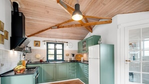 A kitchen with teal cabinets, a white refrigerator, a wooden ceiling, and a window with a view.