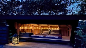 A cozy outdoor sleeping area with a bed, pillows, and a lantern.