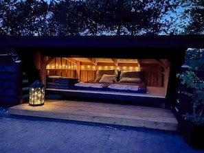 A cozy outdoor sleeping area with a bed, pillows, and a lantern.
