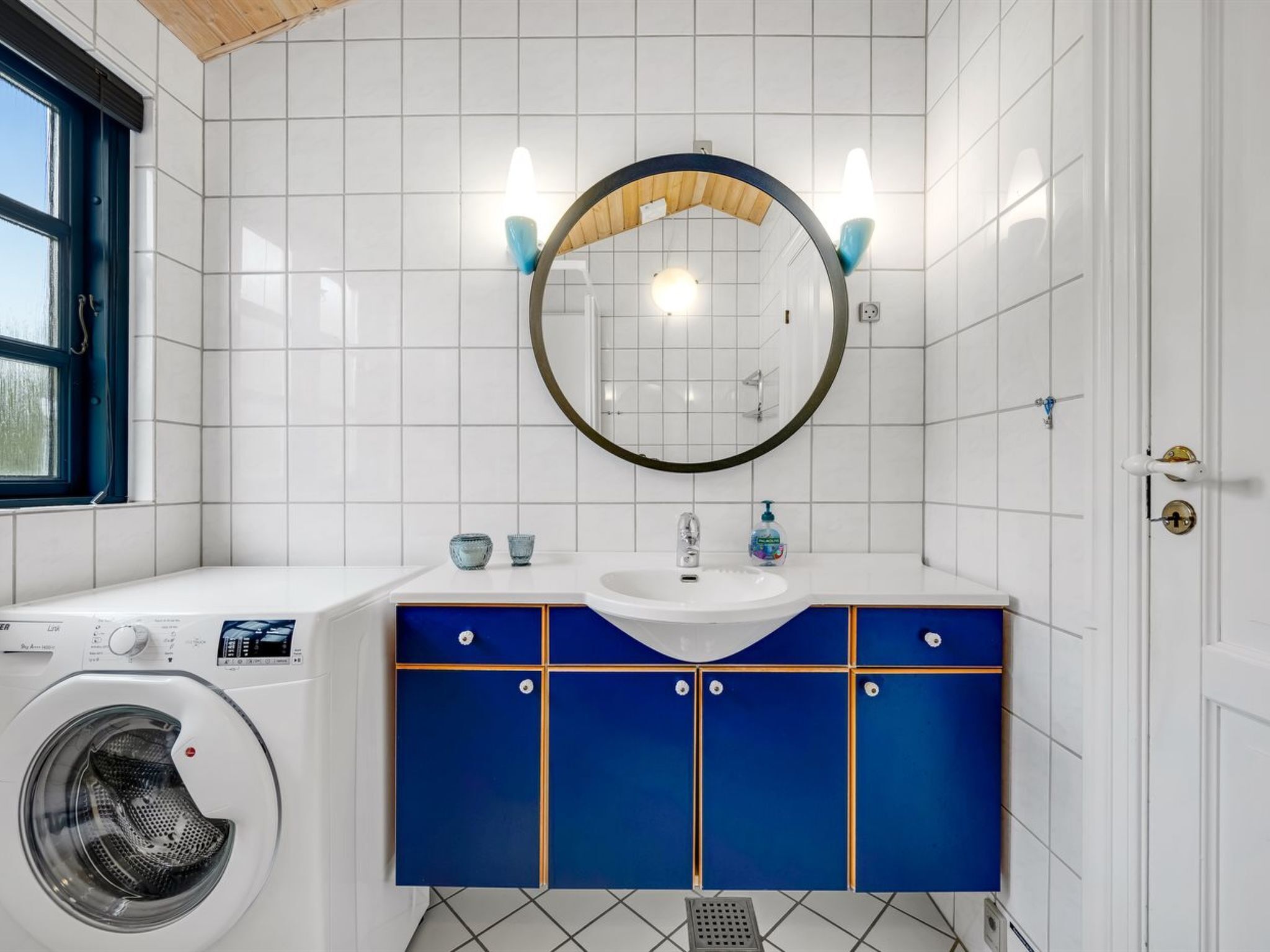 Une salle de bain moderne avec un lave-linge, un lavabo avec un miroir et des meubles bleus.