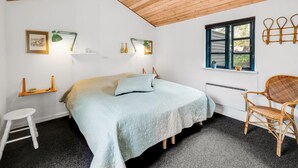 A bedroom with a bed, bedside tables, a chair, a window, and a hanging light fixture.