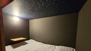 A bedroom with a bed, a nightstand, a shelf, and a star-patterned ceiling. - Guest house cocode. - Hostel (Ishigaki)