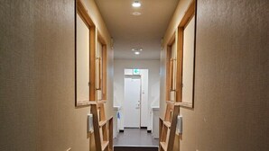 A narrow hallway with wooden paneling and a central staircase leading to a door at the end. - Guest house cocode. - Hostel (Ishigaki)