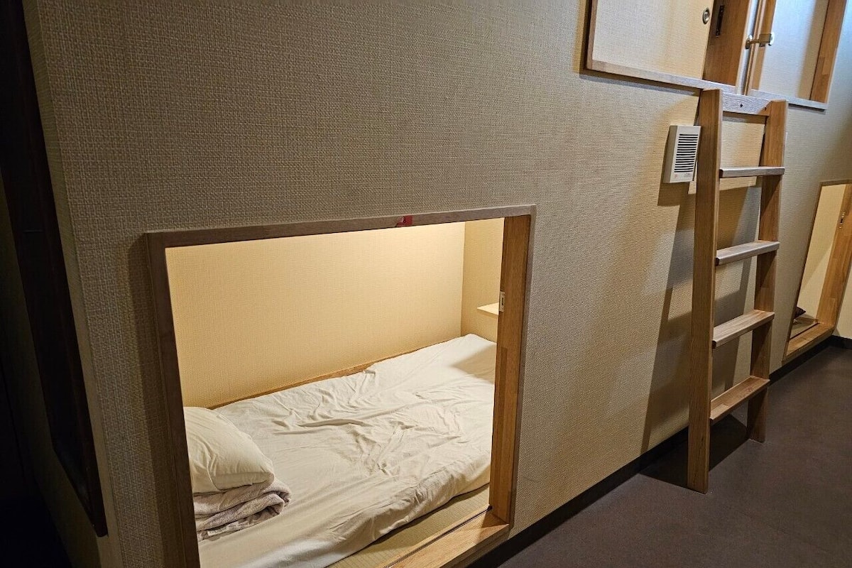 A bunk bed with a ladder and a small shelf, a wall-mounted vent, and a door in a room with a textured wall.