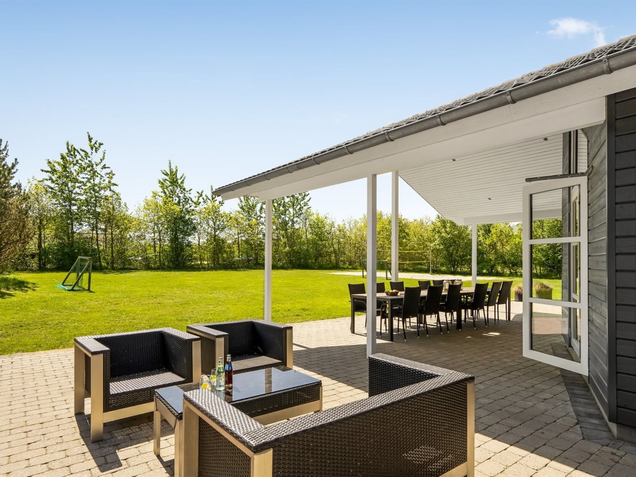 Une terrasse extérieure aménagée avec des meubles en osier, une table et un espace salon abrité.