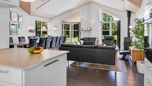 A spacious living area with a large sofa, dining table, and chairs. There is a kitchen area with a stove and a dining table. The room has large windows and a high ceiling with wooden beams. - "Ahto" - 600m to the fjord by Interhome (Højslev)