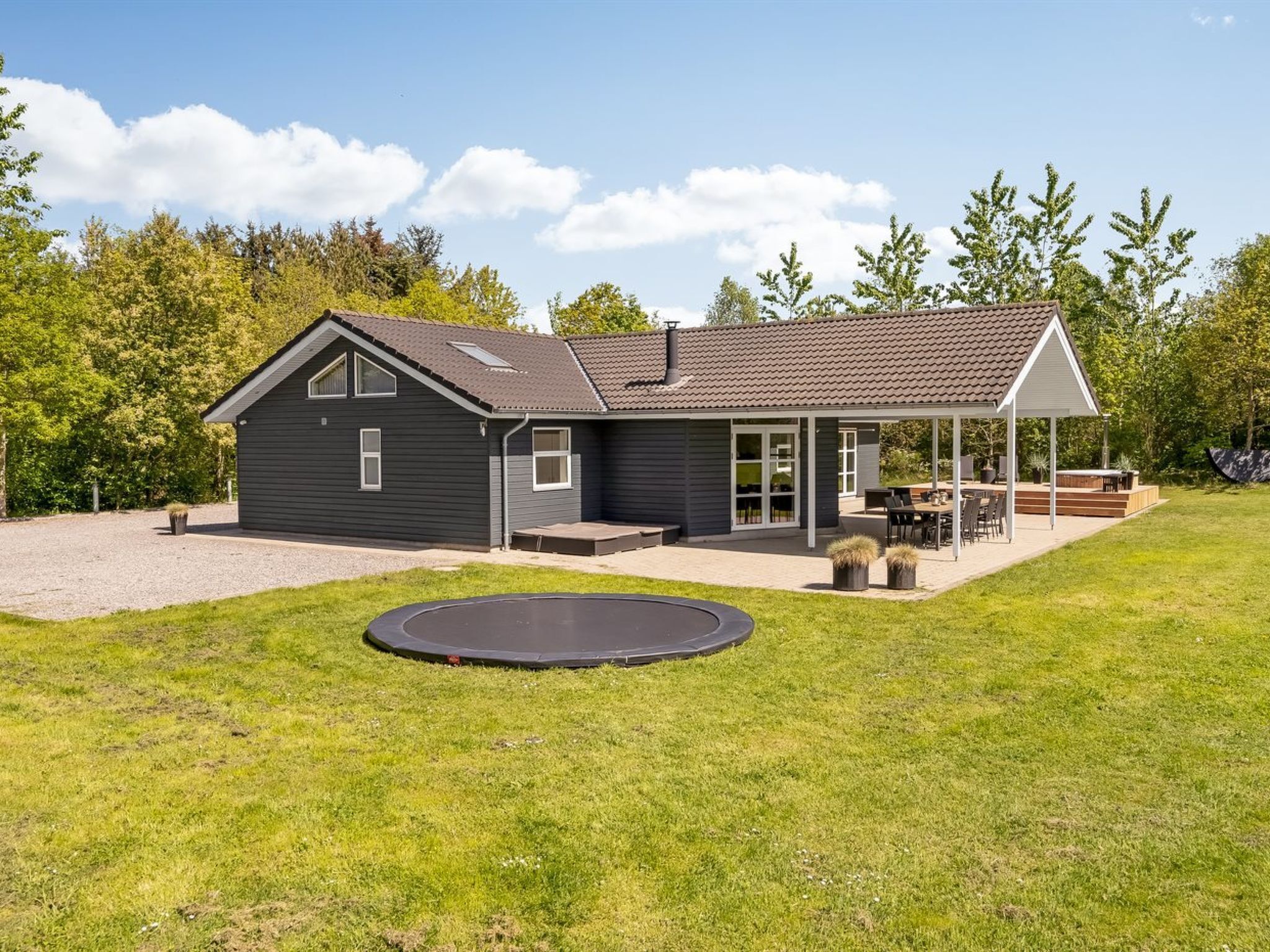 A modern house with a covered patio, a trampoline, and a well-maintained lawn.