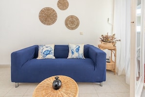 A blue sofa with patterned cushions, a wicker coffee table, and wall decor.