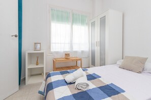 Un dormitorio con una cama, un armario, una mesita con una vela y una ventana con cortinas traslúcidas.