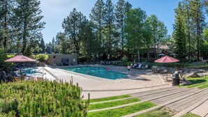 Ein Swimmingpool, umgeben von Liegestühlen und Sonnenschirmen, mit einem kleinen Gebäude und Bäumen im Hintergrund.