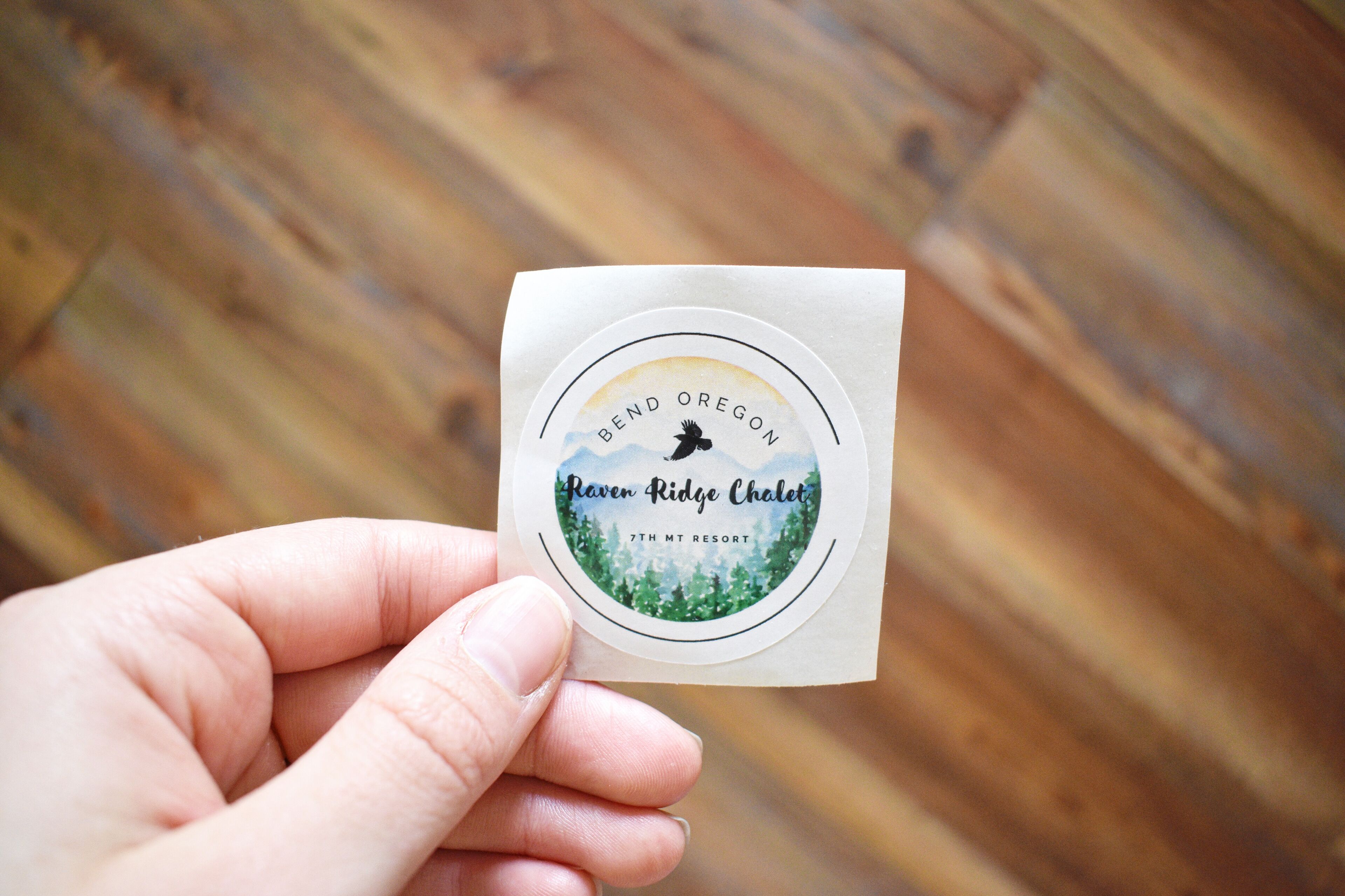 A hand holding a business card with a logo for Bend Oregon Raven Ridge Chalet, 7th Mt Resort.
