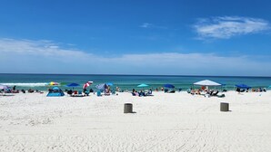 Ein Strand mit weißem Sand, blauen Sonnenschirmen und entspannten Menschen.