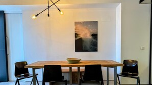 A modern dining area with a wooden table, four black chairs, a hanging light fixture, and a framed picture of a seascape on the wall. - Urban Elegance Close to the Bullring 2BR · 2BA (Sevilla)