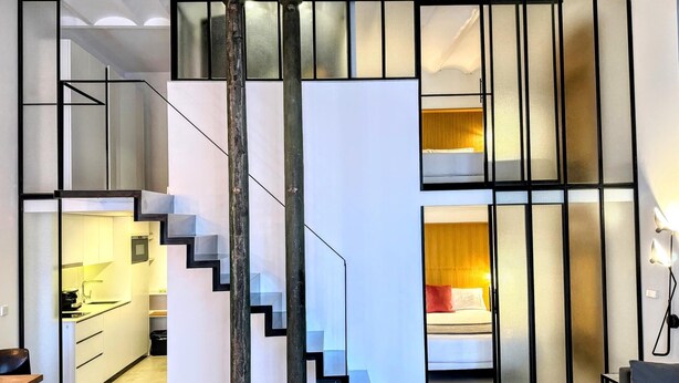 A modern interior with a staircase leading to a loft bedroom, a kitchen area, and a seating area with a sofa. - Urban Elegance Close to the Bullring 2BR · 2BA (Sevilla)