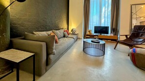 A modern living room with a sofa, a coffee table, a TV, and a chair. - Urban Elegance Close to the Bullring 2BR · 2BA (Sevilla)