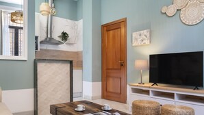 A modern living room with a wooden door, a TV on a wooden stand, a fireplace, and a dining table with two cups. - Sevillian Charm on Sol street - Comfort and Tradition 5 Min from Las Setas (Sevilla)