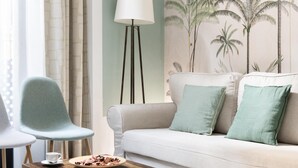 A living room with a sofa, two chairs, a floor lamp, and a wall with a tropical plant mural. - Sevillian Charm on Sol street - Comfort and Tradition 5 Min from Las Setas (Sevilla)