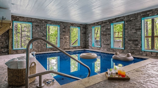 A stone-walled indoor pool with a clear view of trees through the windows.