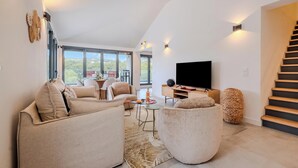 Una sala de estar moderna con sofá, sillón, televisor y una escalera.