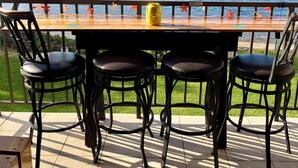 A wooden table with four black chairs, a yellow vase, and a view of the sea and mountains. - Kanai a Nalu Unit 204 Oceanfront Corner Unit- New rate for Summer (Wailuku)