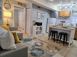 A compact living space with a kitchenette, a sofa with cushions, a patterned rug, and a small dining area with stools. - The Port - Walkable to University of Florida, includes Parking (Gainesville)