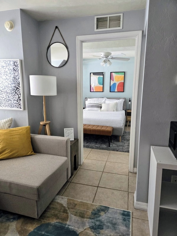 A modern hotel room with a grey sofa, a standing lamp, a framed abstract painting, and a bed with a white duvet. - The Port - Walkable to University of Florida, includes Parking (Gainesville)