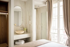Een badkamer met een houten wastafelmeubel, een ronde spiegel, een beige wastafel en een douchegedeelte.