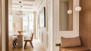 A well-lit hallway with a wooden bench, a dining area with a table and chairs, and a large window with curtains.