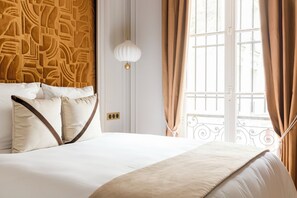 Een hotelkamer met een bed, beige gordijnen, een witte muur en een raam met uitzicht.