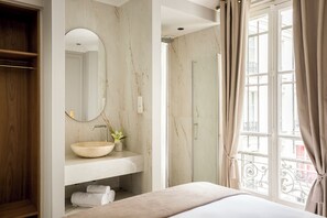 Een badkamer met een marmeren wastafel, een ronde spiegel, een wastafel en een douche.