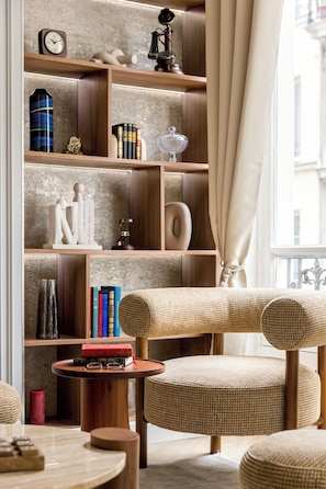 A cozy reading nook with a wooden bookshelf, a vintage rotary phone, and a comfortable chair with a woven seat. - Merveil - Signature Suite - Marais - Caire II (Paris)