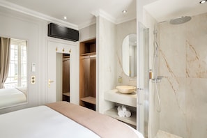 A modern hotel room with a large bed, a walk-in closet, a bathroom with a marble shower, and a vanity with a large mirror. - Merveil - Signature Suite - Marais - Caire II (Paris)