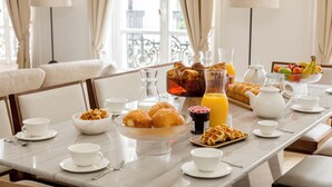 A breakfast setting with a marble table, white cups, bowls, pastries, and a fruit bowl.