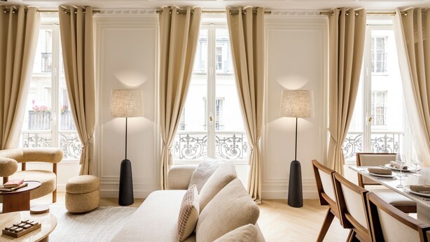 A room with a sofa, chairs, a dining table, floor lamps, and large windows with curtains.