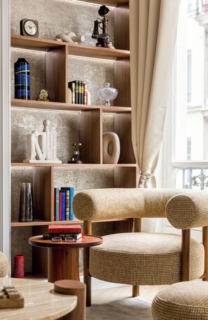 A cozy reading nook with a bookshelf, a round table, and two wicker chairs. - Merveil - Signature Suite - Marais - Caire II (Paris)