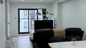 Un salon moderne avec un canapé noir, une table à manger et des chaises. Une grande fenêtre offre une vue sur l’extérieur.