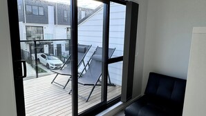Une chambre moderne dotée d’une grande porte-fenêtre coulissante qui donne sur un balcon offrant une vue sur un quartier résidentiel et une voiture garée.