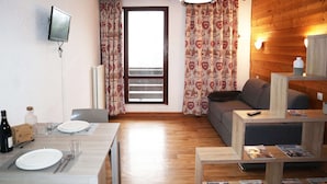Un salon moderne avec un plancher en bois, un coin repas avec une table dressée pour deux personnes, un canapé et une table basse avec des magazines.