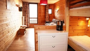 A wooden cabin room with a bunk bed, a white dresser with drawers, a coffee maker on the dresser, a small table with a chair, and a window with curtains. - Studio for 4 people in the heart of the resort of Les Orres 1650 (LES ORRES 1650)